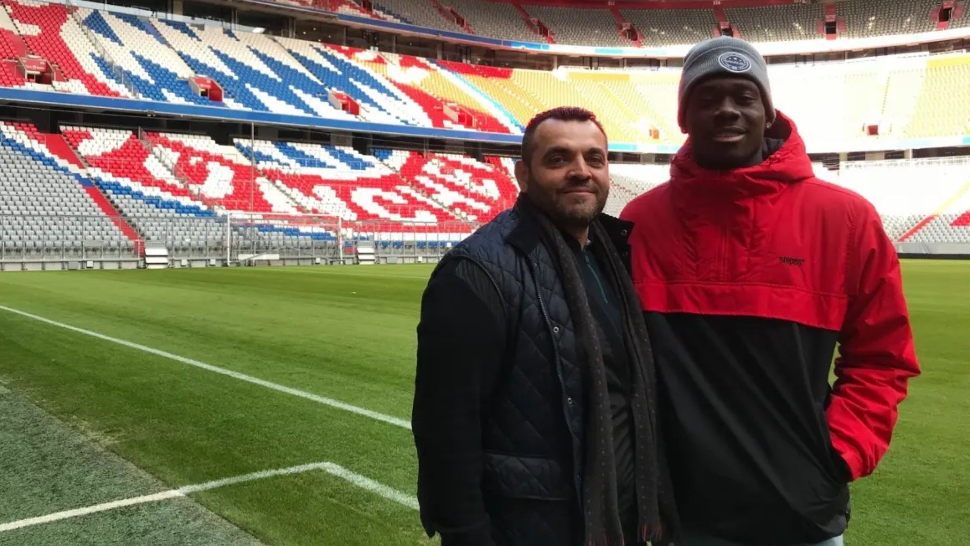 Alphonso Davies con su representante, Nedal Huoseh, posan sobre el césped del Allianz Arena.
